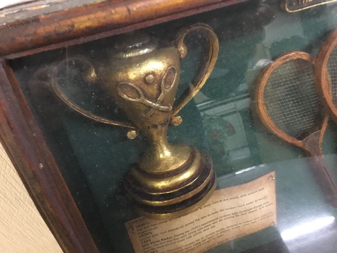 アンティークなテニスラケットの歴史と変遷について解説している彫刻が収められた額装